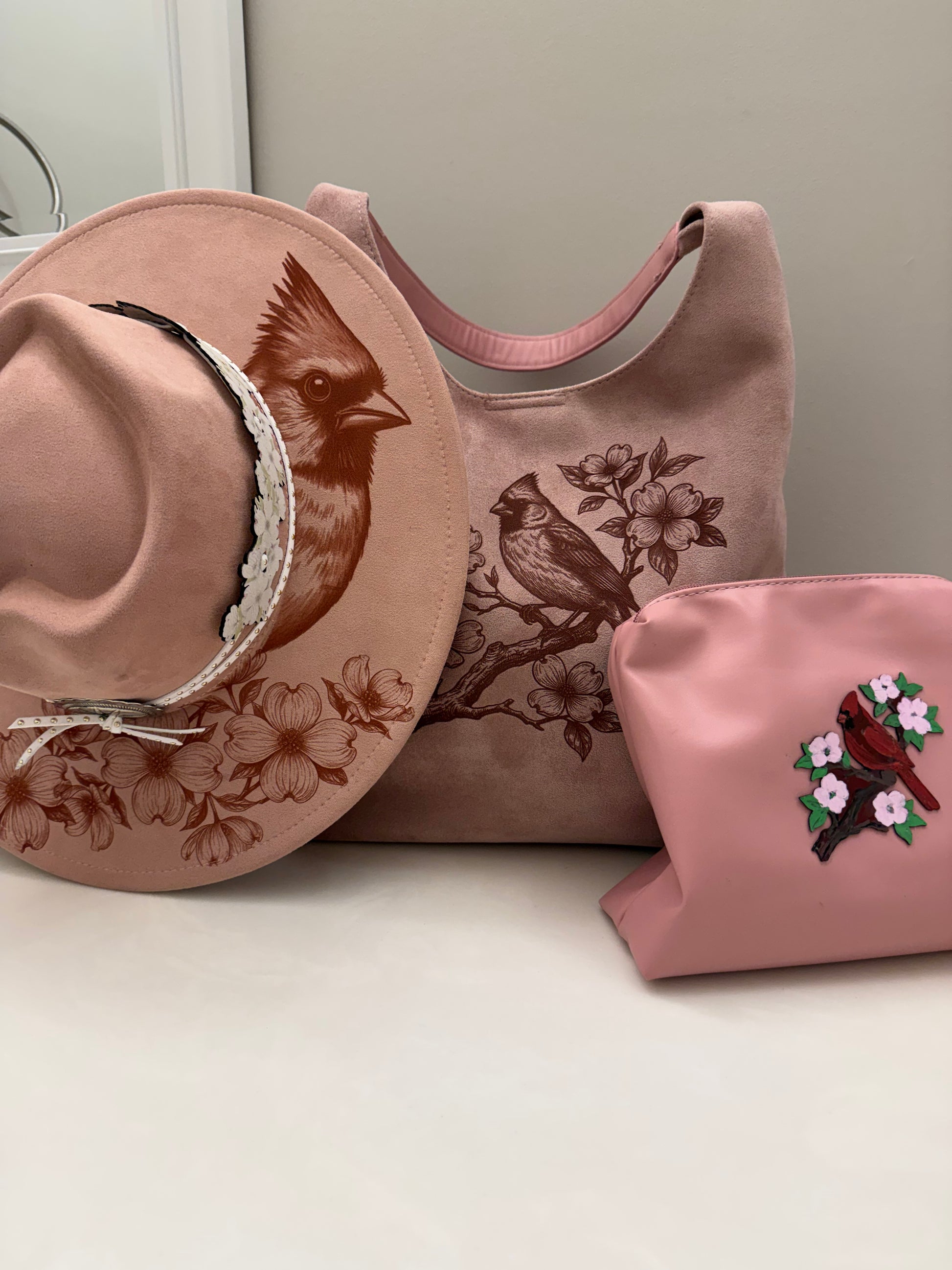 Beautiful cardinal hanging out on a branch of a Dogwood tree made by Beach Vibes NC/Crystal Coast Cowgirl Set of 3 items large brim faux suede heart shaped hat, large faux suede pink handbag and makeup bag.