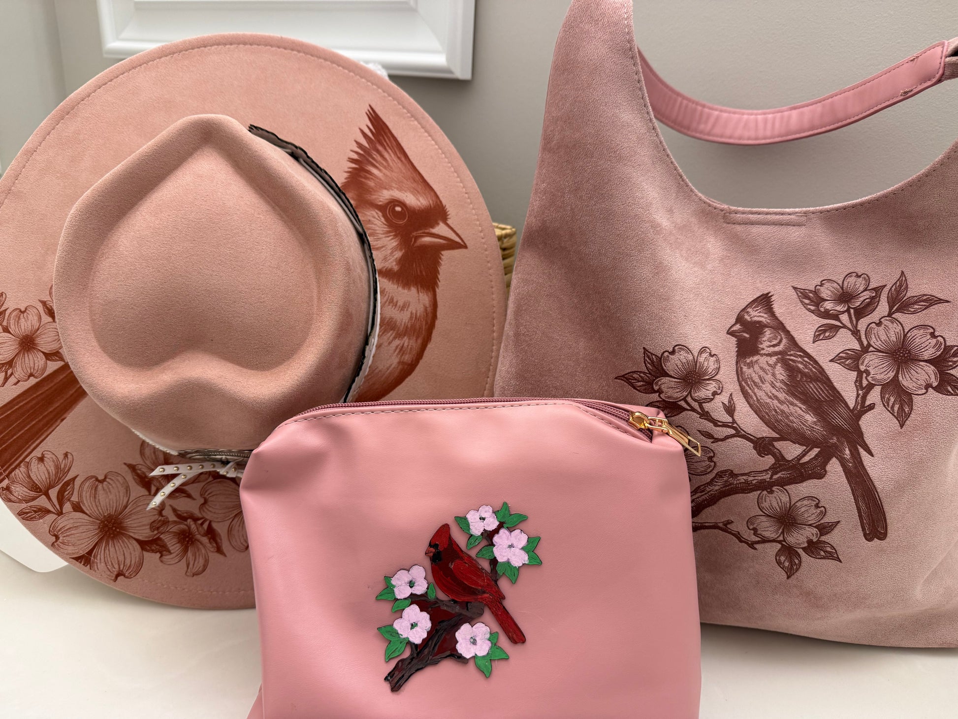 Beautiful cardinal hanging out on a branch of a Dogwood tree made by Beach Vibes NC/Crystal Coast Cowgirl Set of 3 items large brim faux suede heart shaped hat, large faux suede pink handbag and makeup bag.